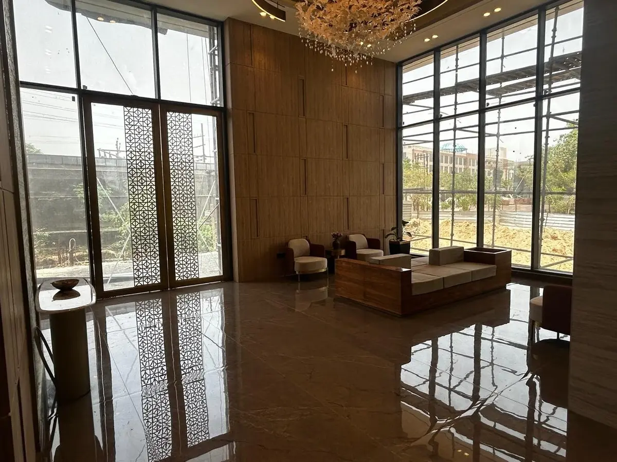 The completed double-height lobby at AIGIN Royal Park photographed on site, with stone-clad walls, a full-height chandelier and lounge seating
