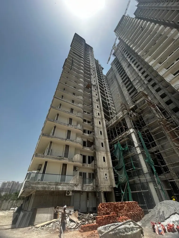 External finishing under way at AIGIN Royal Park, Ghaziabad: scaffolding and green netting up one face of the tower with construction material stacked at ground level