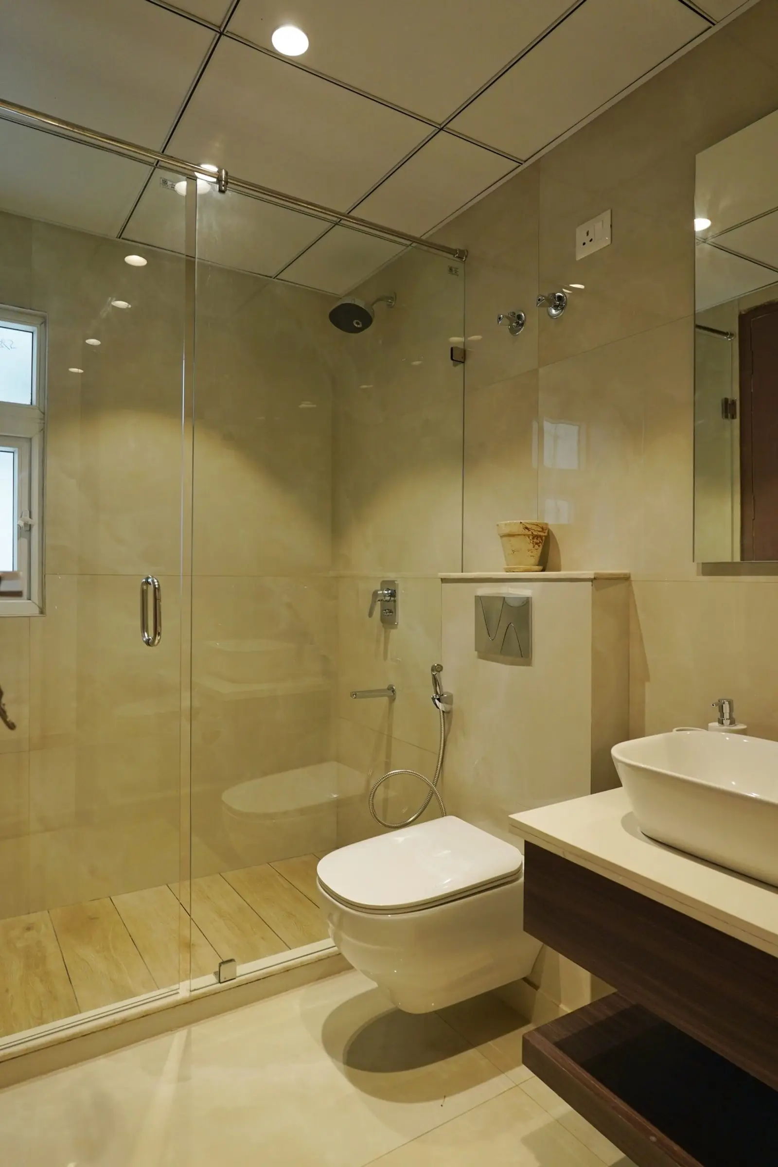 Bathroom with a walk-in glass shower, wall-hung WC and counter-top basin in the sample flat at AIGIN Royal Park, Ghaziabad