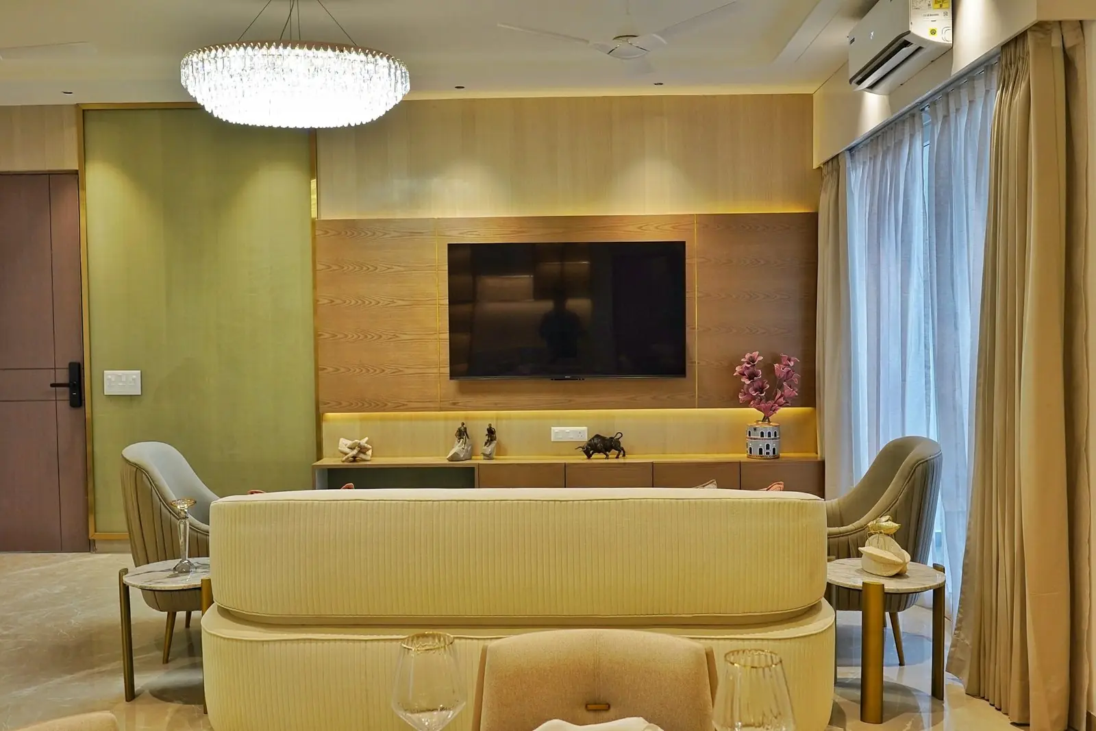 Living room with a panelled television wall and full-height curtained glazing in the sample apartment at AIGIN Royal Park, Ghaziabad